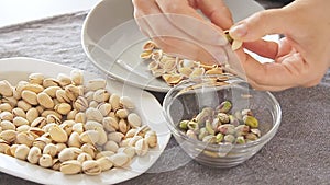 Woman hands opening pistachios above glass bowl