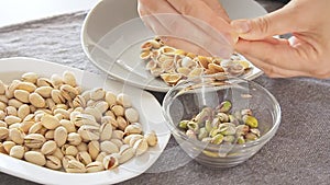 Woman hands opening pistachios above glass bowl