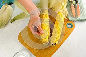 Woman hands peeling ear of corn on cutting board cooking on kitchen at home.