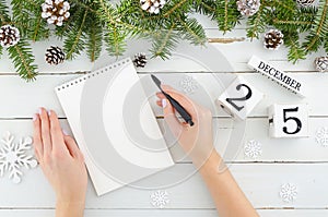 Woman hands with pen and blank notebook. Christmas decoration Fir tree, Pine cones and perpetual calendar 25 december on