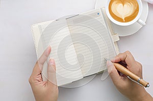 Woman hands with pen writing on notebook and coffee cup on white