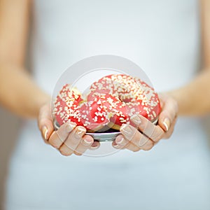 Woman hands with perfect nail polish holding a plate with pink donuts