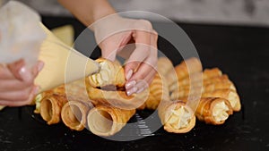 Woman hands pipe the cream into each end of the horn rolls. Woman making puff rolls with cream.