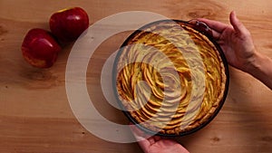 Woman hands places freshly baked French apple pie on wooden table, top view. Apple tart serving