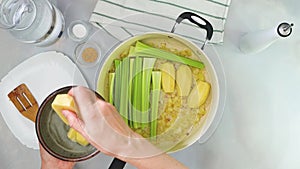 Woman hands placing raw potatoes in a pot.Creamy pureed celery soup