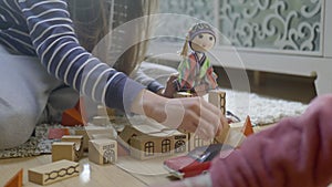 Woman hands playing with wooden blocks and a doll, showing kid how to build