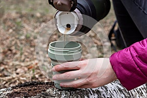 Woman hands pouring tea from thermos into cup. Hot drink break during hiking or camping in autumn or spring time.