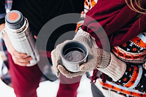 Woman hands pours hot tea or coffee out of thermos on winter forest background. girl using a thermos in on a snowy day. metallic c