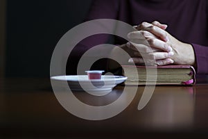 Woman hands in prayer posture on top of open bible with eucharist sacraments on top of table