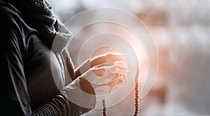 Woman hands praying and holding a beads rosary on lighting backgrouns, black&white, religious faith concept