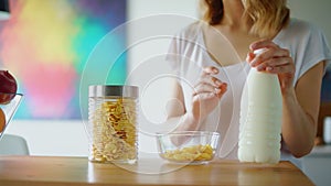 Woman hands preparing cereals with milk on kitchen table