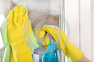 Woman hands in protective gloves cleaning window with rag and cleanser spray at home