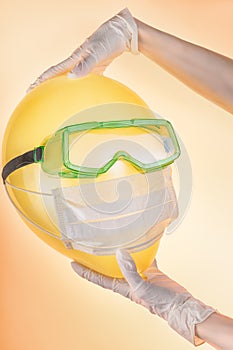 Woman hands in protective gloves holding balloon in safety glasses and medical mask