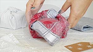 Woman hands puts Furoshiki eco-friendly gift wrapped in cloth on a table
