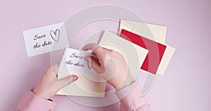 Woman hands putting save the date card in the envelope. Wedding planning, invitation concept