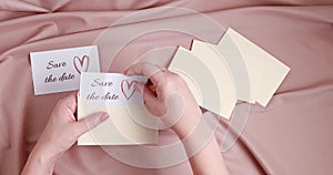 Woman hands putting save the date card in the envelope. Wedding planning, invitation concept