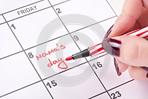 Woman hands with red felt pen writes words Mamas day in calendar