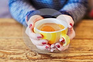 Woman hands with red manicure and cup of fresh hot coffee on wooden table