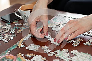 Woman hands with red nail polish putting jigsaw puzzle pieces together.