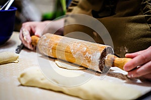 Woman hands rolling out dough in flour with rolling pin in her home kitchen. Selective focus