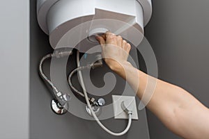 Woman hands setting temperature of water in heater electric boiler. Interior details close-up.