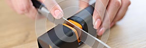 Woman hands sharpen knife with sharpener on kitchen table close-up.