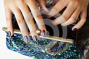Woman hands with shiny manicure holding little purse peacok feather, cosmetic and fashion people concept