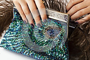 Woman hands with shiny manicure holding little purse peacok feather, cosmetic and fashion people concept