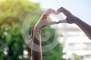 Woman hands showing heart shape sign with LGBTQ Rainbow ribbon in the morning for Lesbian, Gay, Bisexual, Transgender and Queer