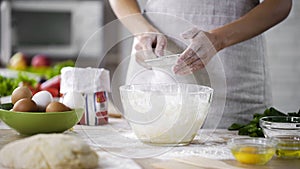 Woman hands sieving flour over glass bowl with dough, adding baking ingredients