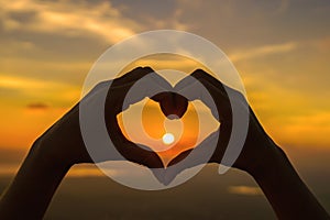 Woman hands silhouette on beautiful sunset above the mountain in the form of love heart-shaped hand gesture Concept of love, life