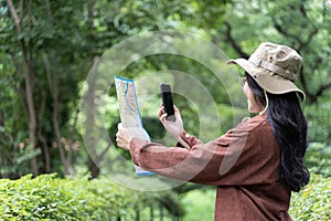 Woman hands with a smartphone and map in the forest background, isolate screen. Happy young woman with a map, smartphone