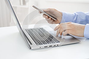 Woman hands with smartphone using laptop at workplace or home