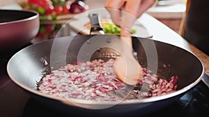 Woman hands sweat or saute onions in frying pan stirring with wooden spoon