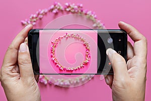 Woman hands takes flower wreath photo from mobile smart phone or cell phone digital camera