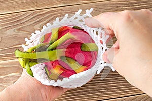 Woman hands taking dragon fruit or pitaya from market packaging foam mesh on a brown wooden table. Healthy vegetarian food rich in