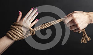Woman hands tied with a coarse rope close-up black background