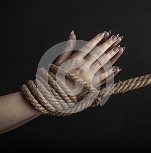 Woman hands tied with a coarse rope close-up black background