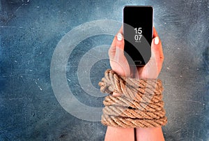 Woman hands tied with rope on a concrete background suggesting internet or social media addiction or captivity.