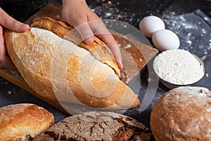 Woman hands touching white wheat bread on wooden board with bowl of flour and two eggs blue table