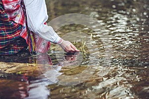 Woman hands in traditional shirt, touching water in the river