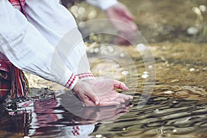 Woman hands in traditional shirt, touching water in the river