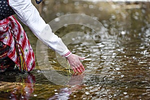 Woman hands in traditional shirt, touching water in the river