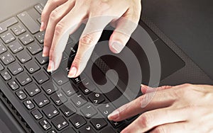 Woman hands typing on black laptop keyboard, close up detail from above