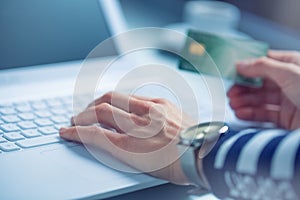 Woman hands typing on the keyboard of laptop holding credit card