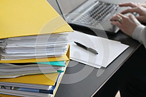 Woman hands typing on laptop computer with binders filled with papers in foreground. Selective focus