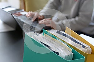 Woman hands typing on laptop computer with binders filled with papers in foreground. Selective focus