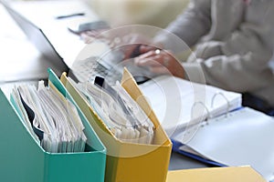 Woman hands typing on laptop computer with binders filled with papers in foreground. Selective focus