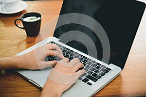 Woman hands typing laptop computer with blank screen on table in coffee shop.