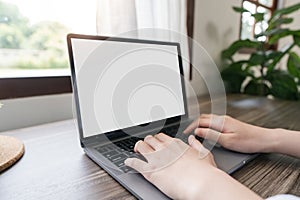 Woman hands typing on the laptop with empty blank white screen mockup. Computer is laying on the table. Person working